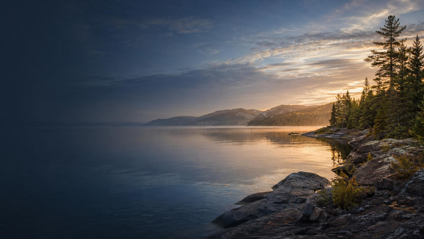 A calm Canadian lake surrounded by evergreen forest and mountains